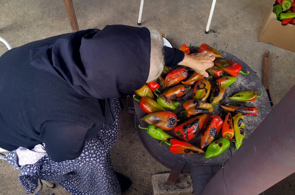 grandmother with black veil roasting peppers on a wood burned stove