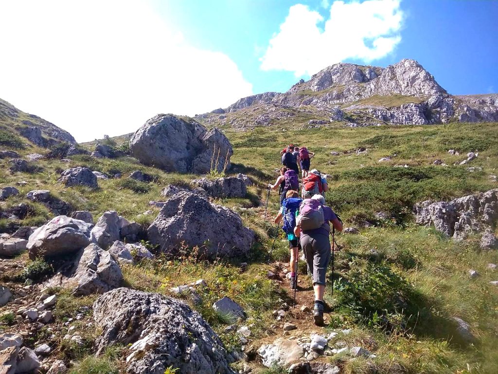eight middle-aged people with full gear hiking on a rocky trail